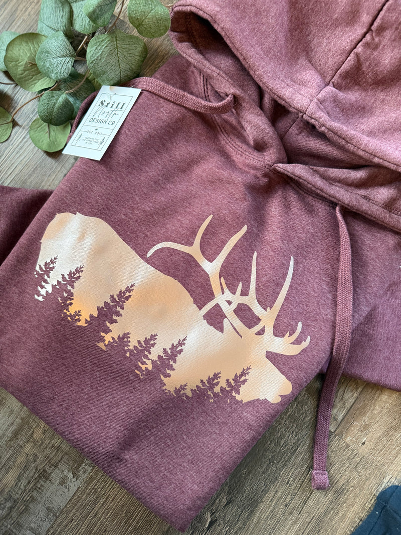 Close-up of the elk and evergreen forest graphic on the Dusty Rose Elk Hoodie
