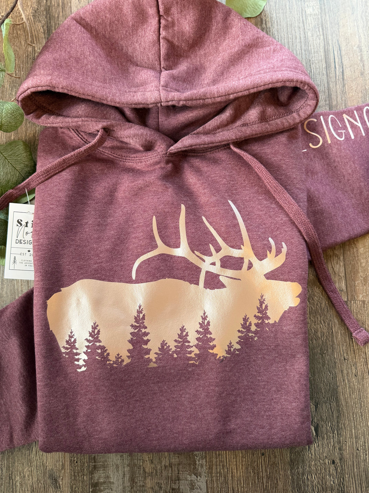 Dusty rose unisex hoodie with an elk silhouette and evergreen forest graphic, front view